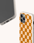 Two Brown Checker Eco-Friendly Phone Cases are shown: one shows the screen, the other displays the back with an orange and beige checkerboard pattern. Made of textured, biodegradable material.
