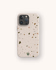 A Brown Terrazzo Eco-Friendly Phone Case, featuring small, multicolored specks and a small green “U” at the bottom center, is displayed on a smartphone against a plain off-white background.