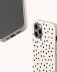 The Black Hearts Eco-Friendly Phone Case features a cream color with a speckled texture and small scattered black hearts. Made from sustainable materials, it is shown from both the front and back.