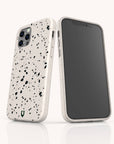 Two smartphones in Black Terrazzo Eco-Friendly Phone Cases, one showing the screen and the other displaying the back with three cameras, standing upright on a white surface with a beige background.