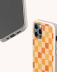 Two smartphones in Brown and Orange Checker Eco-Friendly Phone Cases—one displays the screen and charging port, while the other shows an orange-yellow checkerboard patterned triple camera case. Compatible with iPhone and Samsung Galaxy.