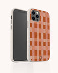 The Terracotta Watercolour Checker Eco-Friendly Phone Case, featuring a red and pink checkered pattern, stands upright to display both its sustainable design and the smartphone's front screen.