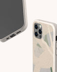 Two smartphones with Green Abstract Lines Eco-Friendly Phone Cases in beige, featuring subtle green and cream abstract designs. One shows the front and charging port; the other reveals the back with three camera lenses and side buttons.