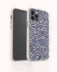 The Ocean Waves Eco-Friendly Phone Case, shown in beige with a wavy navy blue ocean-inspired pattern, stands upright to display its biodegradable back design and the screen facing left.