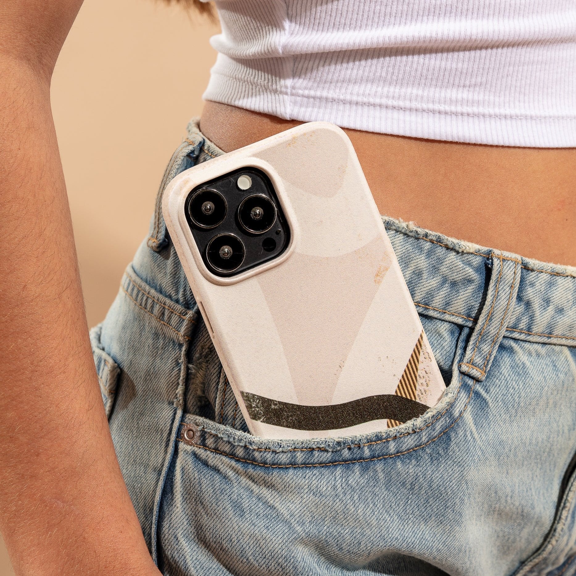 A person in a white crop top and blue jeans has a Beige Abstract Eco-Friendly Phone Case, made from biodegradable materials and compatible with iPhone and Samsung Galaxy, sticking out of their front jeans pocket.