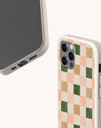 Two smartphones in Pink and Green Checker Eco-Friendly Phone Cases—one shows the screen and charging port, the other features a pastel pink, beige, green, and peach checkerboard pattern. Compatible with iPhone and Samsung Galaxy.