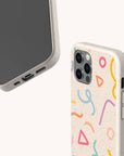 Two smartphones in light beige Confetti Eco-Friendly Phone Cases—one with colorful abstract shapes, one plain—are shown at angles revealing sides and corners. Compatible with iPhone and Samsung Galaxy models.