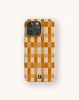 The Brown Watercolour Checker Eco-Friendly Phone Case features a tan and brown checkerboard pattern with a small dark green horseshoe icon near the bottom center. It has an off-white background and fits compatible iPhone and Samsung models.
