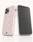 Two smartphones with the Pink Ditsy Flowers Eco-Friendly Biodegradable Phone Case are displayed—one shows the floral pattern, the other a blank screen. Both cases stand upright on a reflective white surface, ideal for eco-conscious buyers.