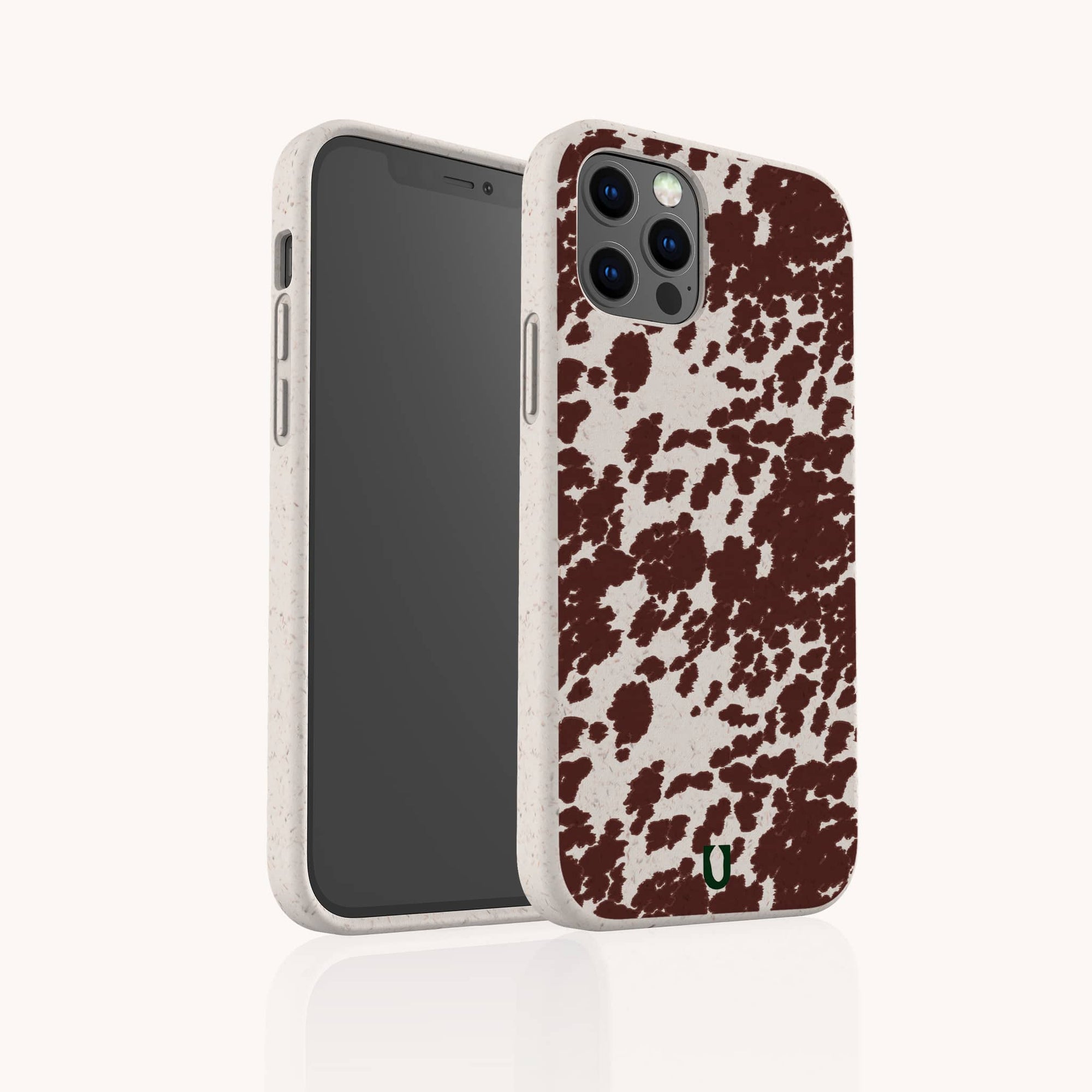 The Brown Cow Print Eco-Friendly Phone Case is shown on a smartphone, featuring a speckled beige edge, small green logo at the bottom, and compatibility with iPhone and Samsung Galaxy models. Both front and back of the phone are displayed.