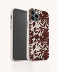 The Brown Cow Print Eco-Friendly Phone Case is shown on a smartphone, featuring a speckled beige edge, small green logo at the bottom, and compatibility with iPhone and Samsung Galaxy models. Both front and back of the phone are displayed.