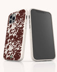 Two smartphones with matching Brown Cow Print Eco-Friendly Phone Cases are displayed. The off-white cases feature a brown cow print pattern on the back and precise camera cutouts. One phone, an iPhone, is shown facing forward, while the other, a Samsung Galaxy, displays the back of its case.