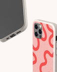 Two smartphones in speckled beige Red and Pink Swirl Lines Eco-Friendly Phone Cases; one displays the screen and charging port, while the other shows a pink and red swirl pattern on the back with three camera lenses. These biodegradable cases are compatible with both iPhone and Samsung devices.