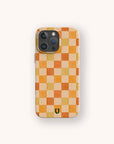 The Brown and Orange Checker Eco-Friendly Phone Case features orange, yellow, and beige squares with a green horseshoe logo at the bottom. Compatible with iPhone and Samsung Galaxy models.