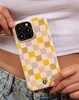 A person in a white crop top and denim jeans holds a phone with the Pink and Purple Checker Eco-Friendly Phone Case near their waist.