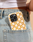 A Star Terracotta Checker Eco-Friendly Phone Case, featuring a yellow and white checkered design, is tucked into the back pocket of light blue jeans. A person wearing a white ribbed crop top is partially visible.