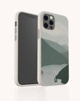 The Blue Watercolour Landscape Eco-Friendly Phone Case, shown from the back and side against a light background, features a beige-speckled biodegradable design with a minimalist blue watercolour mountain and lake scene.