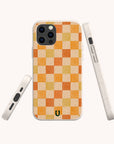 The Brown and Orange Checker Eco-Friendly Phone Case is shown from three angles—back, side, and bottom. Featuring compostable materials, a small green horseshoe detail, and compatibility with iPhone and Samsung Galaxy.