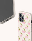 Two beige phone cases are featured. One showcases the screen and charging port, while the other displays the Pink Cherries Eco-Friendly Biodegradable Phone Case, adorned with a delightful pattern of pink cherries and green stems on a light background. This sustainable phone case is a stylish choice that’s gentle on the planet.