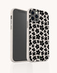 A white Black Flower Power Eco-Friendly Phone Case, featuring a black floral pattern of small, simple flowers, is shown on a smartphone angled to display both its back and screen against a plain white background.
