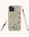The Grunge Eco-Friendly Phone Case in beige with urban black splatter is shown from the back, side, and bottom. Cutouts fit camera, buttons, and charging port. A small green horseshoe logo features at the bottom center.