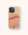 The Hills Eco-Friendly Phone Case in beige features abstract wavy layers in pink, orange, yellow, and tan, plus a green U-shaped logo near the bottom. Compatible with iPhone and Samsung Galaxy models.