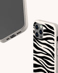 Two Zebra Eco-Friendly Phone Cases are displayed: one shows the front with a plain screen, and the other reveals a black-and-white zebra stripe pattern on the back. Both have beige edges, camera cutouts, and are eco-friendly.