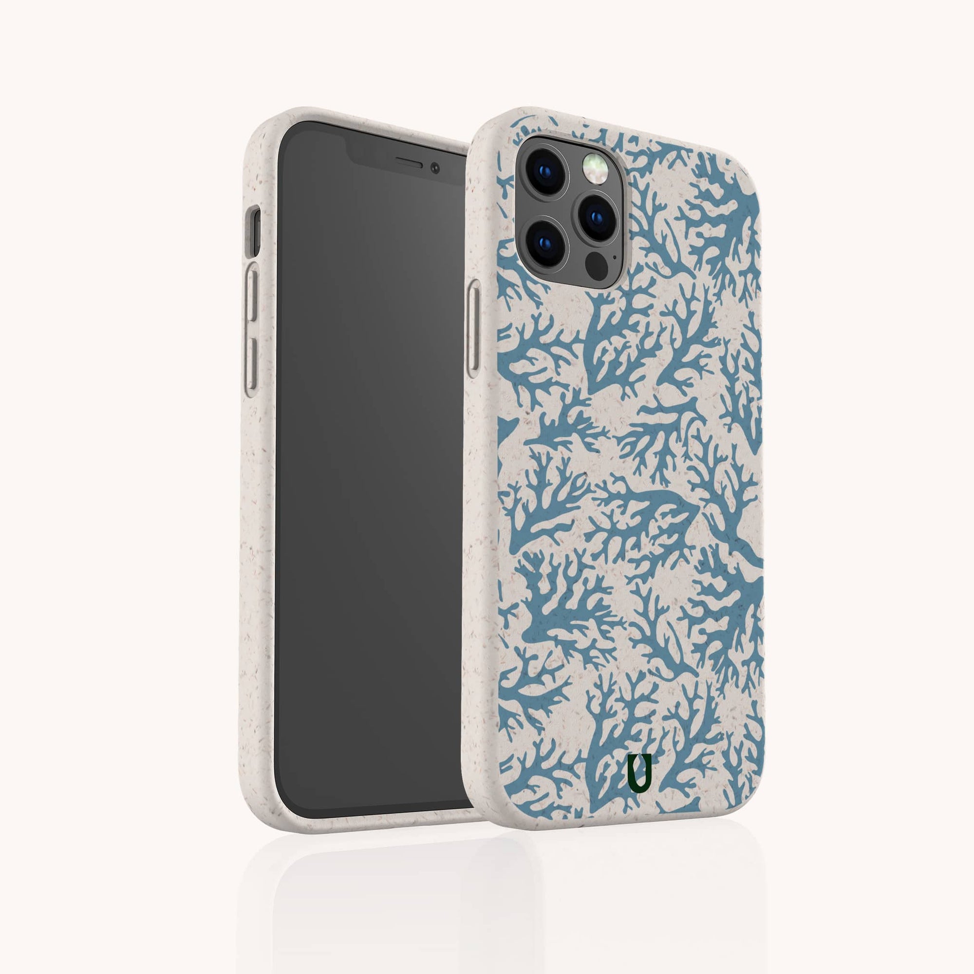 The Blue Coral Eco-Friendly Phone Case is beige with a marine-inspired blue coral pattern and a small green logo at the bottom. Seen upright on a smartphone, it displays both the screen and its biodegradable, decorated back.