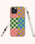 A smartphone with a vibrant checkered case in pink, orange, green, blue, and purple is displayed from the back and sides against a light background. This striking Colour Checker Eco-Friendly Phone Case is available for both iPhone and Samsung Galaxy models.