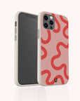 The Red and Pink Swirl Lines Eco-Friendly Phone Case features a pink, biodegradable design with bold red wavy lines, speckles, and a black "U" logo near the bottom. It fits iPhone and Samsung Galaxy models. The phone screen is black and turned off.