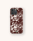 The Brown Cow Print Eco-Friendly Phone Case, compatible with iPhone and Samsung Galaxy, features irregular brown splotches on white and a small green horseshoe near the bottom, shown against a plain light background.