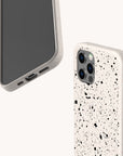 Two smartphones feature the Black Splatter Eco-Friendly Phone Case in off-white with a black paint splatter design; one displays the screen and the other the back. These compostable cases suit iPhone and Samsung. Minimal, light background.