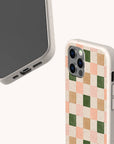 Two smartphones in eco-friendly phone cases are displayed against a light background; one features the Pink and Green Checker Eco-Friendly Phone Case with a checkered pattern in pink, beige, apricot, and green, while the other has a plain design.
