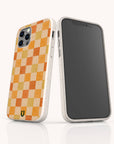 Two smartphones with beige cases are displayed; one showcases the Brown and Orange Checker Eco-Friendly Phone Case, featuring a vibrant yellow and orange checkerboard pattern and a small green horseshoe logo at the bottom, while the other phone shows a blank screen. Both cases highlight their eco-friendly design.