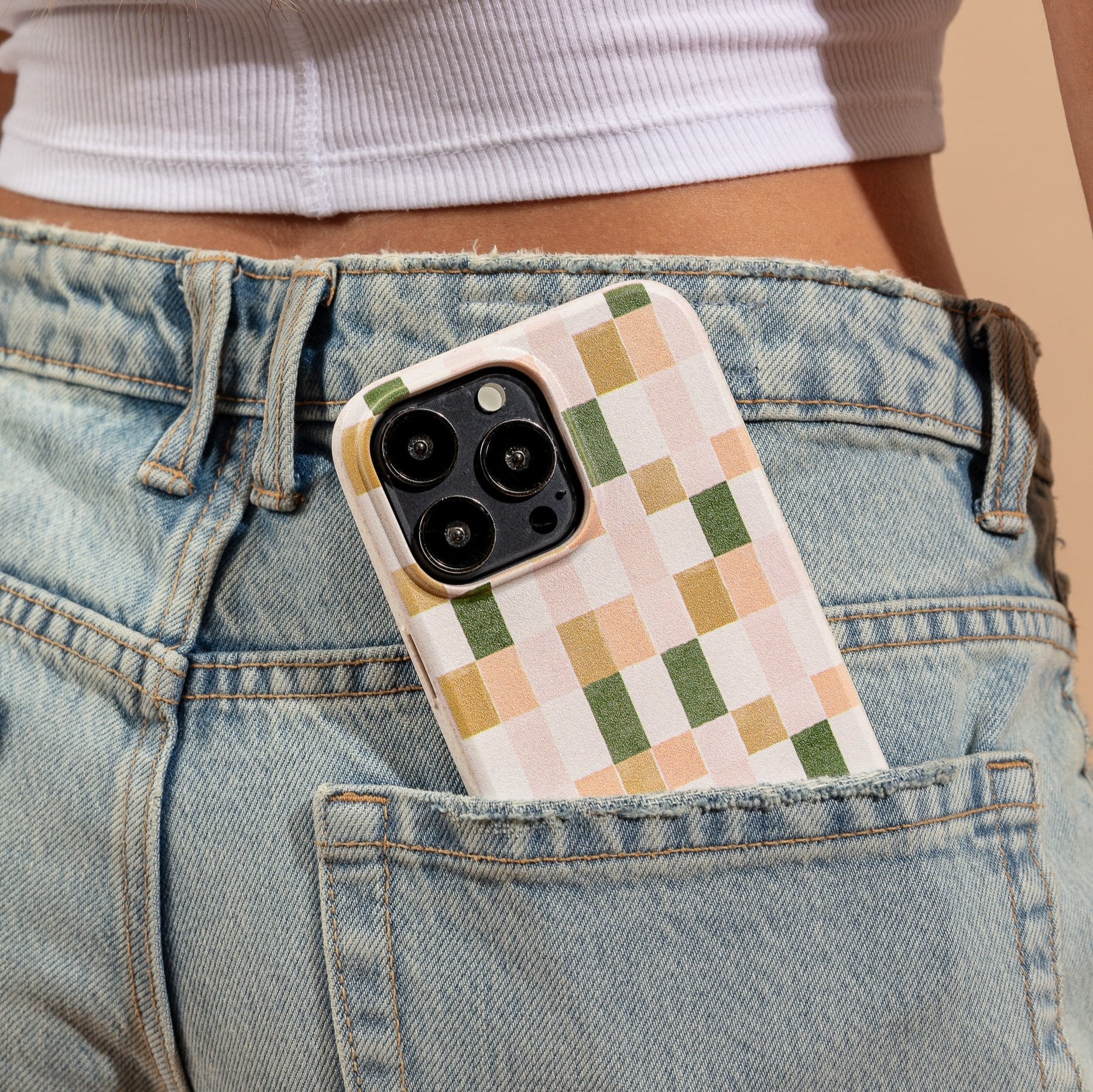 A Pink and Green Watercolour Eco-Friendly Phone Case, made from compostable materials, peeks out of the back pocket of light blue denim jeans worn by someone in a white crop top.