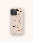 Introducing the Terrazzo Print Eco-Friendly Phone Case: an earth-conscious smartphone accessory featuring a terrazzo pattern of scattered brown, tan, and pink specks. This stylish case is adorned with a small green U logo near the bottom center and offers sustainable protection for your phone.