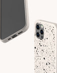 Two smartphones with Black Splatter Eco-Friendly Phone Cases are shown on a light background. Each white case features a bold black paint splatter design; one phone displays its screen, while the other highlights the camera and side buttons.