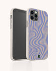 A smartphone with a Blue Distort Lines Eco-Friendly Phone Case stands upright on a light background. The beige and purple wavy striped case, compatible with both iPhone and Samsung models, features a small green logo near the bottom.