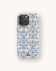 A smartphone with the Blue Ditsy Flowers Eco-Friendly Biodegradable Phone Case, which features a repeating pattern of small blue and green flowers on a white background, viewed from the back.