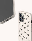 Two smartphones fitted with beige Xo Xo Eco-Friendly Biodegradable Phone Cases; one case is decorated with a black XO pattern. The phones are positioned to highlight the camera, side buttons, and charging port against a plain white background.