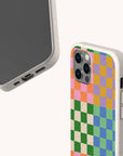 Two smartphones in speckled beige Colour Checker Eco-Friendly Phone Cases—one showing the screen, the other displaying the back with a vibrant pattern of pink, green, yellow, blue, and orange squares. The Colour Checker Eco-Friendly Phone Case is available for both iPhone and Samsung Galaxy models.