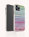 The Winter Rainbow Eco-Friendly Phone Case is shown in speckled white with horizontal pastel stripes in blue, green, purple, and pink—biodegradable and partially turned to display its sustainable style from both the front and back.