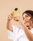 A woman in a white shirt holds up her smartphone with the Star Terracotta Checker Eco-Friendly Phone Case, featuring yellow and white checks, as she looks at the screen against a plain beige background.