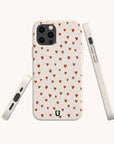 The Red Hearts Eco-Friendly Phone Case, in beige with small red heart patterns and a green U-shaped logo at the bottom, is shown from various angles. It has precise cutouts and fits iPhone and Samsung Galaxy models.