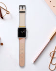 The Abstract Cut Out Vegan Leather Apple Watch Band, featuring a beige, cruelty-free faux leather strap, is placed on a flat surface alongside a pair of glasses, a closed notebook, a gold pen, and two large paper clips in an elegantly arranged display.
