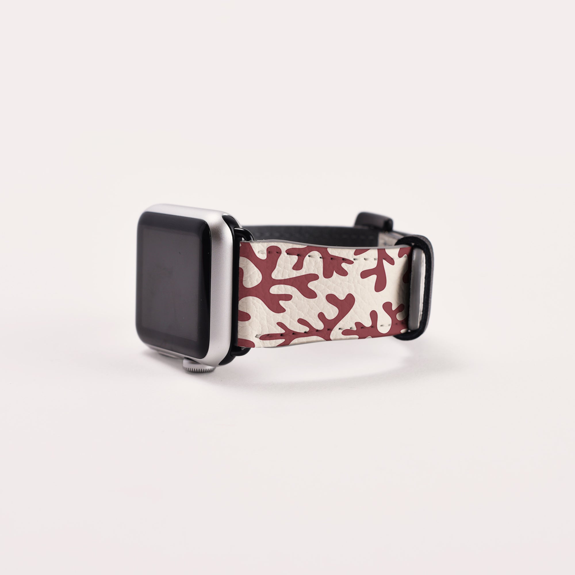 Introducing the Brown Coral Vegan Leather Apple Watch Band, featuring a silver bezel and an eco-friendly strap adorned with an abstract red and white design. Displayed on a light, neutral background, the watch band is angled to showcase its unique strap pattern.