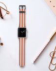 A smartwatch featuring a Brown and Pink Stripes Vegan Leather Apple Watch Band rests on a desk surrounded by office supplies such as a pen, glasses, a notebook, and large paper clips, all set against a pristine white background.