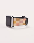 This Apple Watch band, known as the Brown and Purple Checker Vegan Leather Band, showcases a multicolored checker-patterned strap crafted from vegan leather in shades of beige, pink, and orange. Elegant sustainable craftsmanship meets modern design against a plain white background.