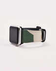 A Green Abstract Lines Vegan Leather Apple Watch Band, showcasing a black front and a distinctive two-tone wristband crafted from vegan leather with dark green and beige sections, is angled slightly on a plain white surface.