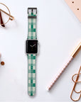 A Green Watercolour Checker Vegan Leather Apple Watch Band is featured on a desk with office supplies like a pen, paper clips, a gold-tipped notebook, and glasses—ideal for eco-conscious art lovers who prioritize style and sustainability.